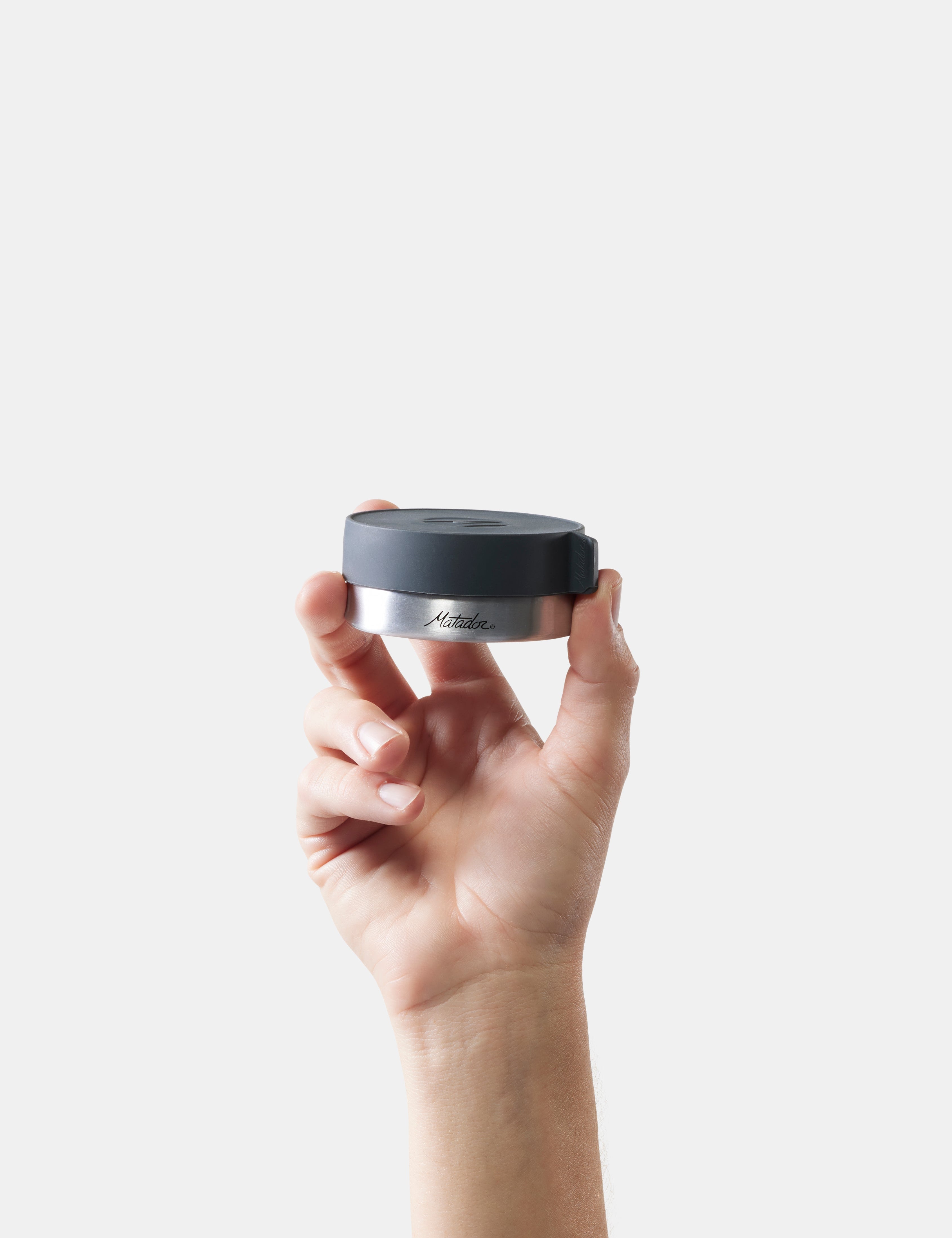 Hand holding a black and silver container with 'Matador' branding against a white background