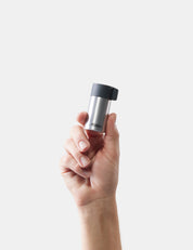Hand holding a silver and black container against a white background