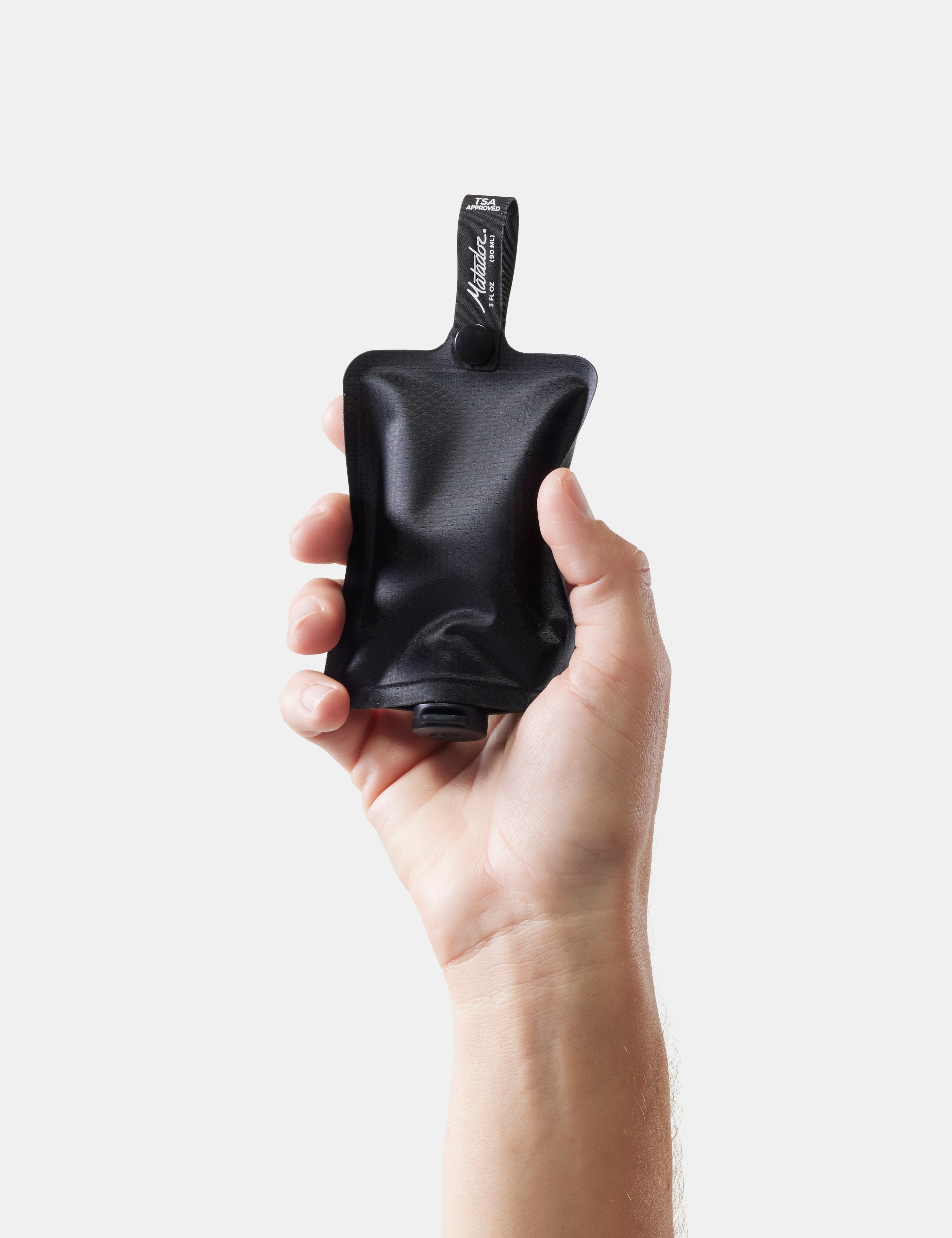 Hand holding a black toiletry bottle with a brand label on a white background