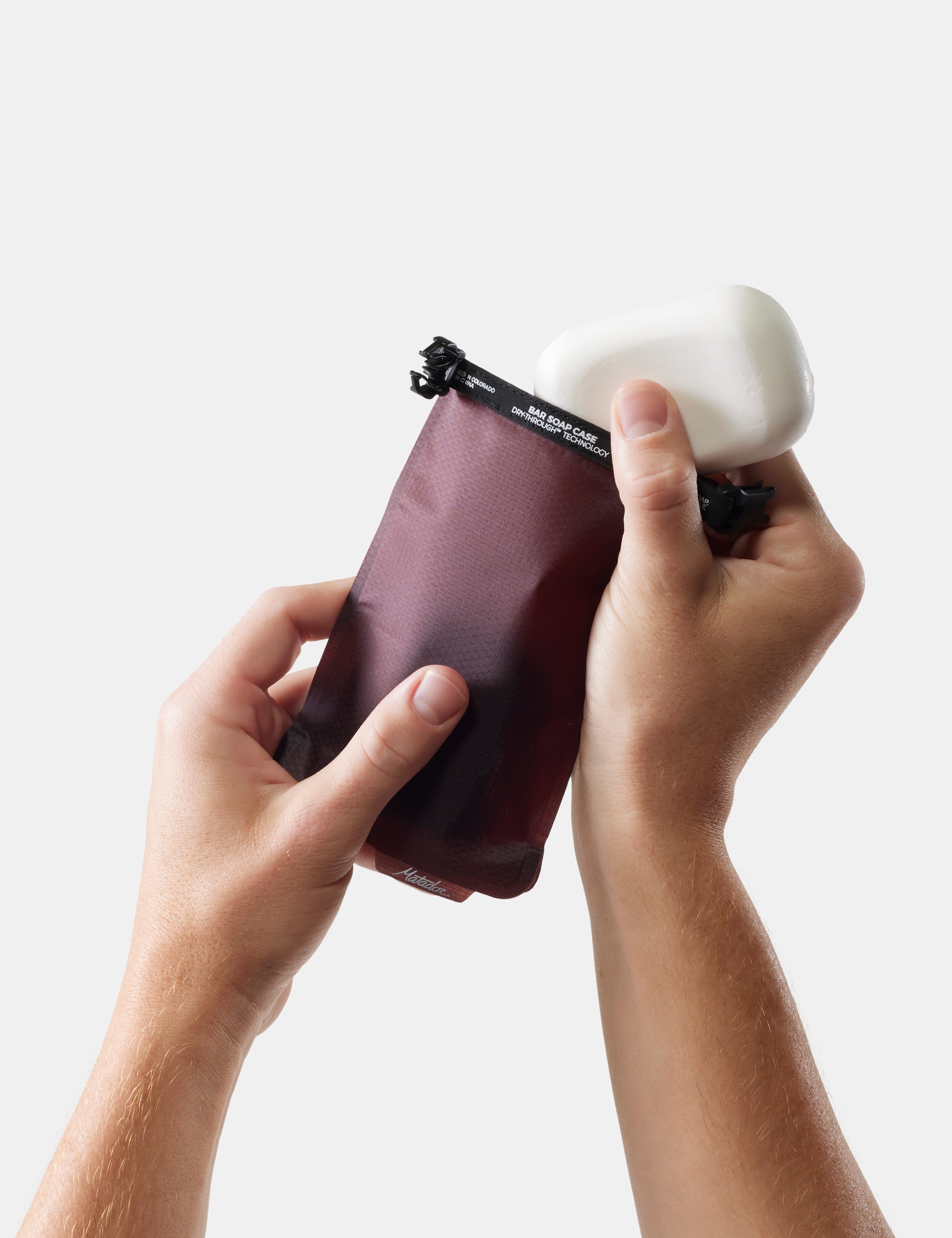hands placing soap into garnet soap bar case on white background