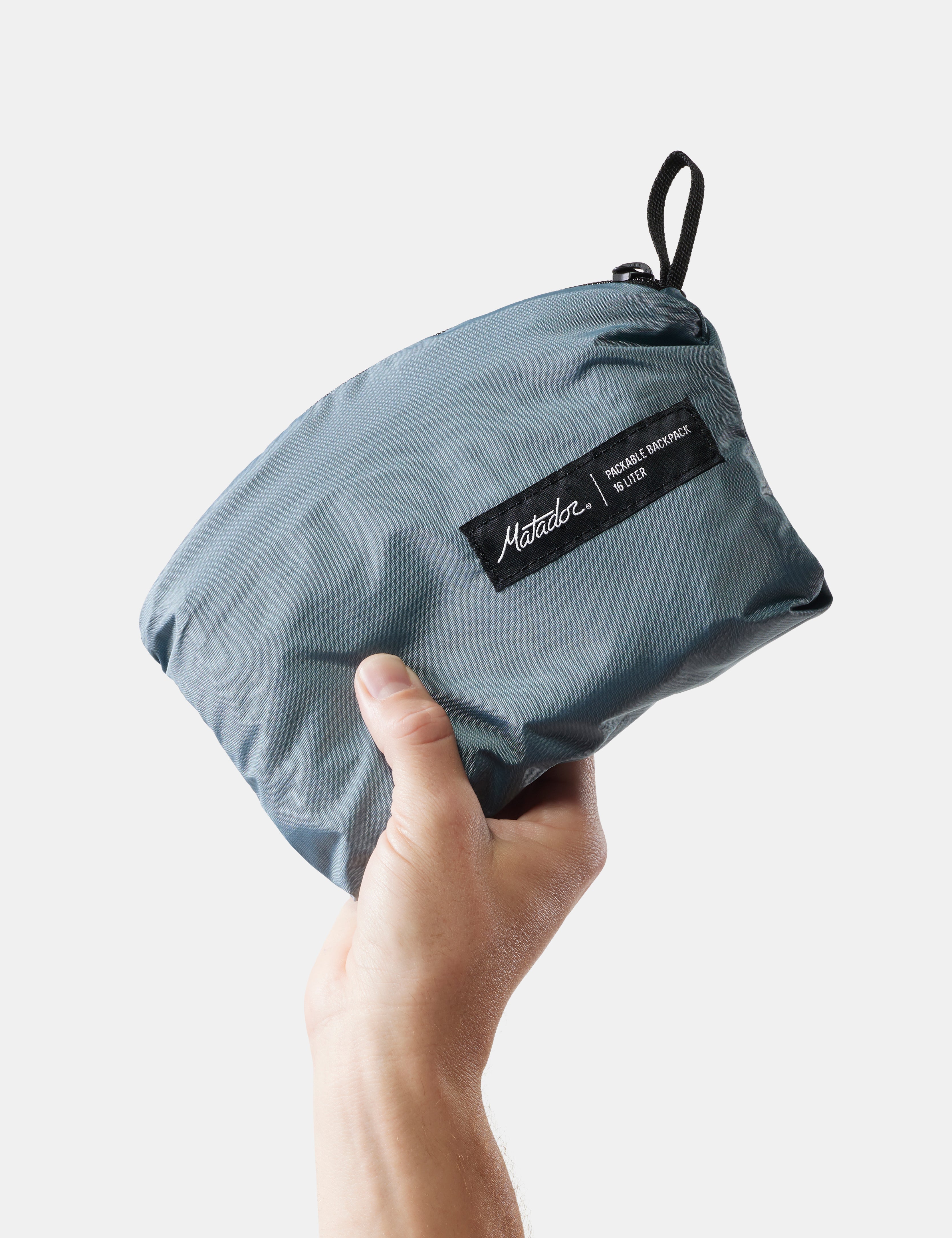 Hand holding a blue pouch with a brand label on a white background